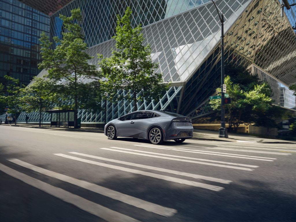 2024 Toyota Prius XSE Premium in Guardian Grey driving through a modern cityscape with geometric glass buildings.