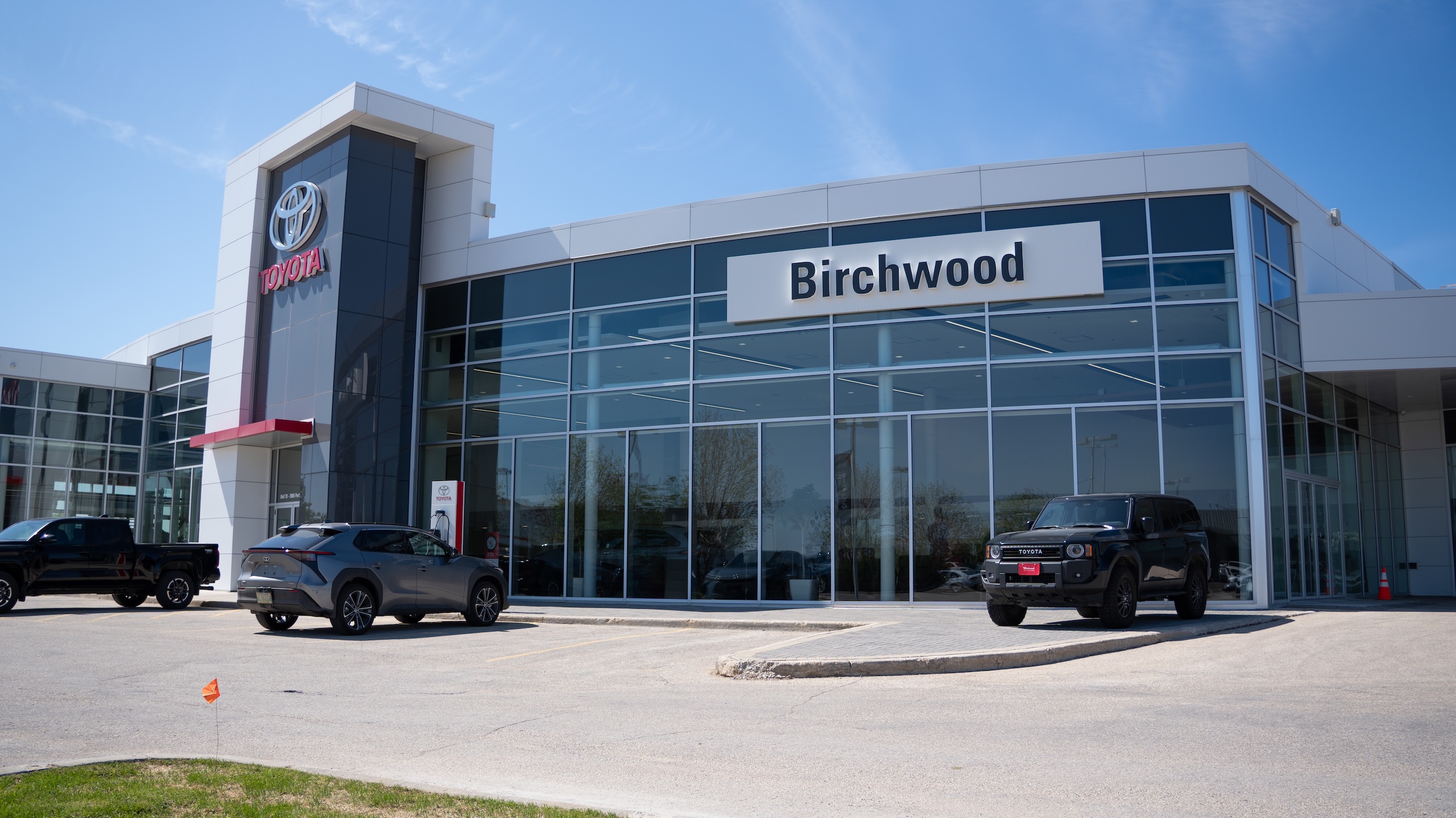 Front view of Birchwood Toyota dealership with bold Toyota signage, modern glass entrance, and two Toyota vehicles parked out front including a black SUV and a grey crossover.